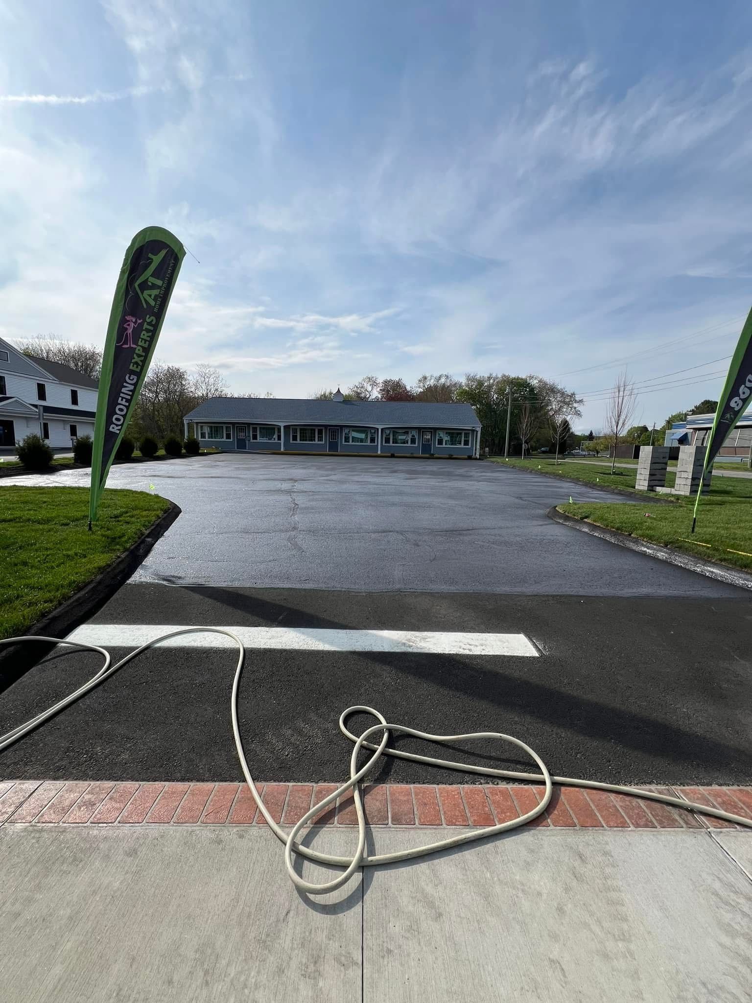 A freshly paved black asphalt parking lot leading to a building, with white guide ropes and green banners on the sides.