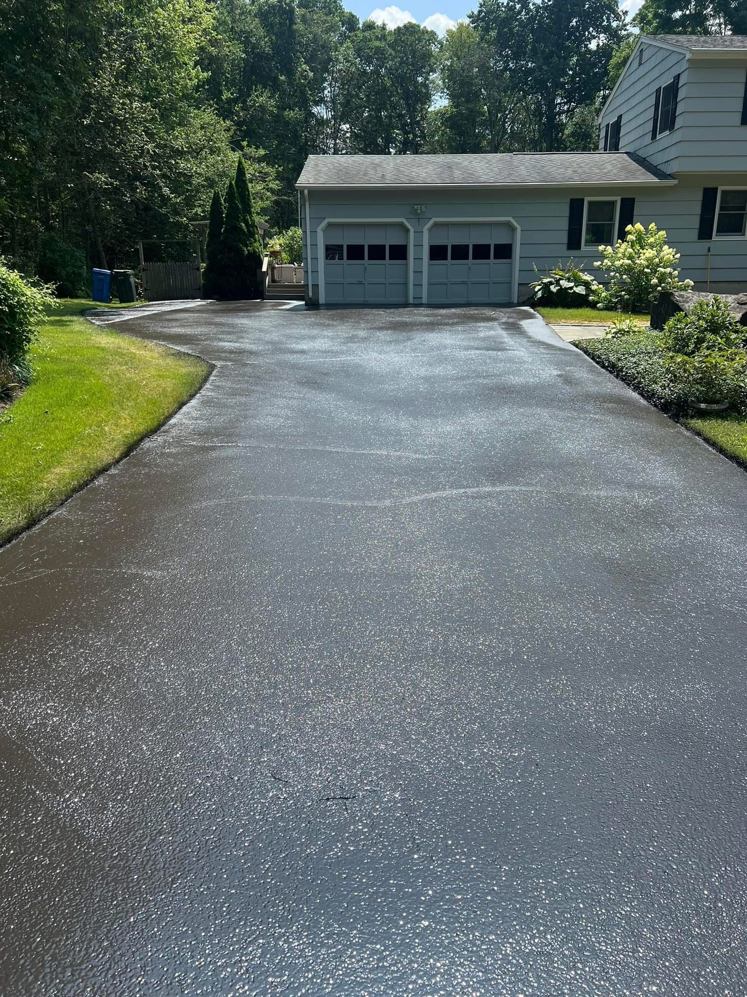 A paved driveway covered in a thin layer of white hail pellets, leading up to a two-car garage of a suburban house.