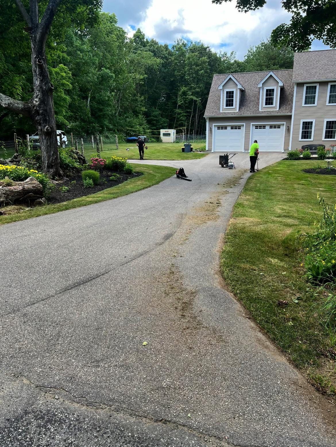 Workers landscaping a front yard and gravel driveway next to a two-story home with a white garage.