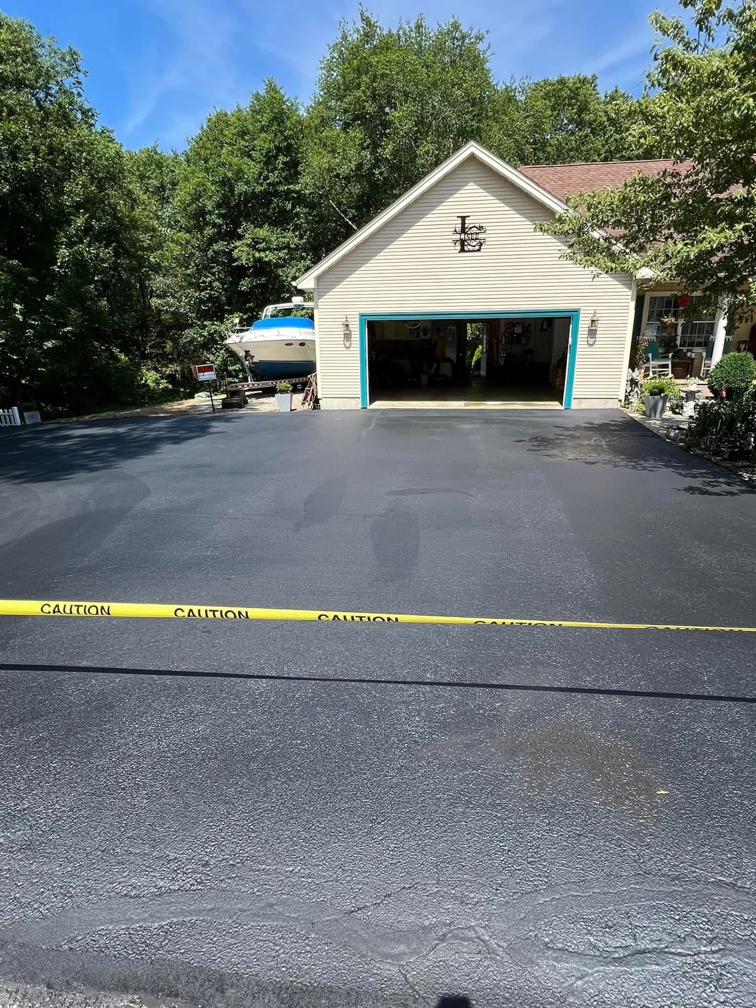 A freshly paved asphalt driveway leads to a garage, blocked off by yellow caution tape.