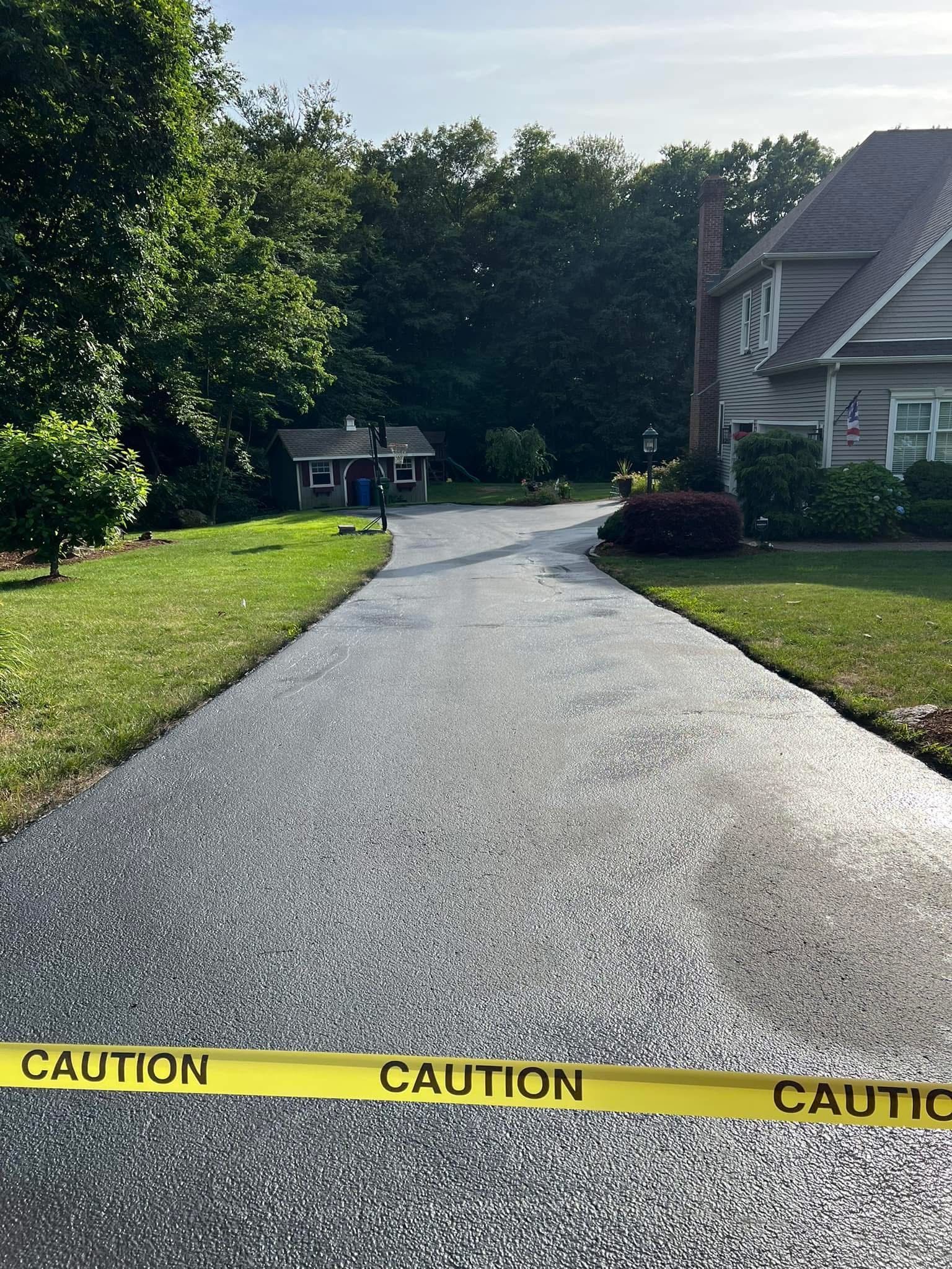 A freshly paved asphalt driveway leading to a house, blocked off by a yellow 