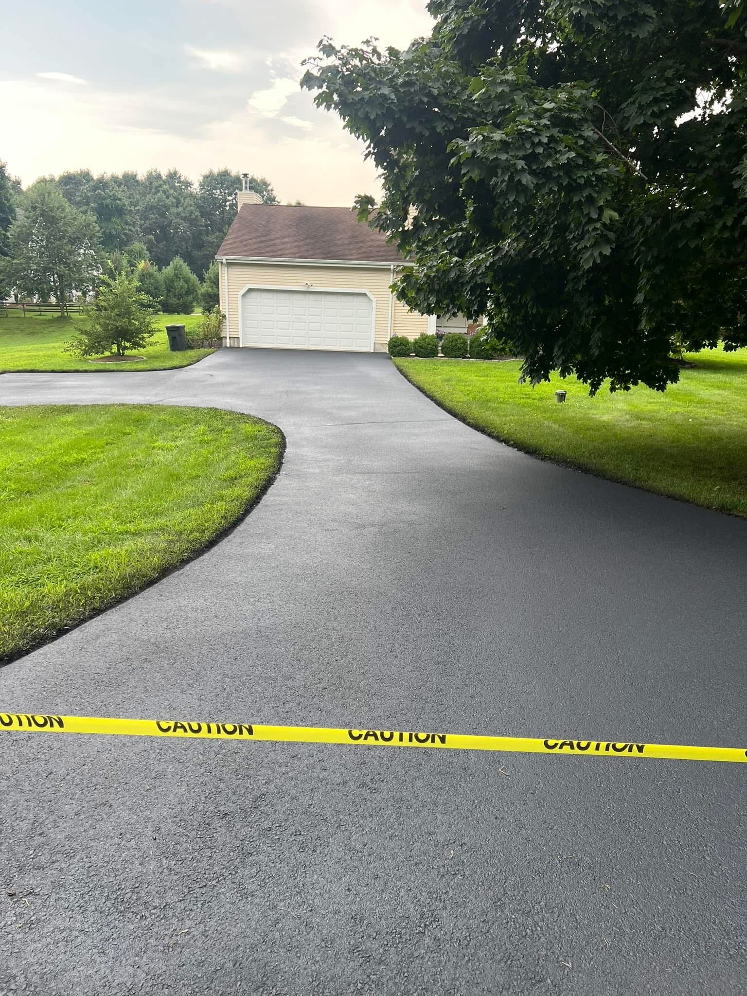 A newly paved asphalt driveway leads to a detached garage, marked off with a yellow caution tape in the foreground.