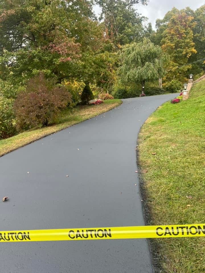 A newly paved asphalt driveway curves through a residential yard, blocked by yellow 