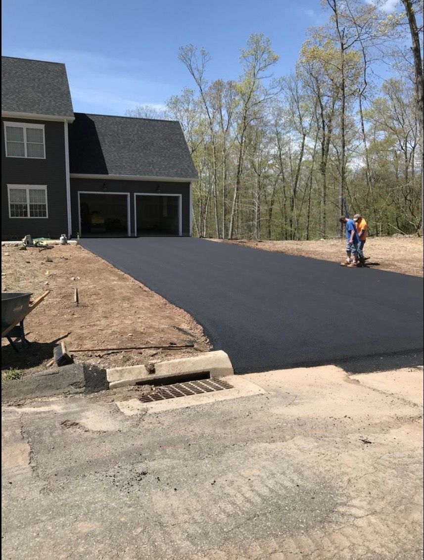 Newly paved black asphalt driveway leading to a two-car garage of a dark-sided house with a person standing nearby.