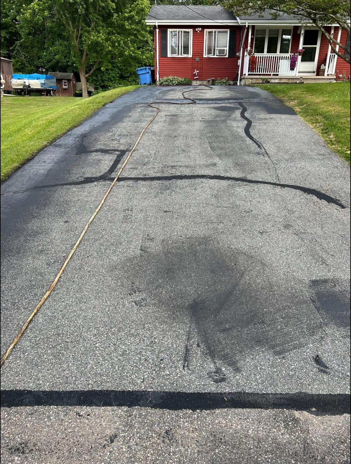 A residential asphalt driveway with cracks repaired with black sealant, leading to a red house.