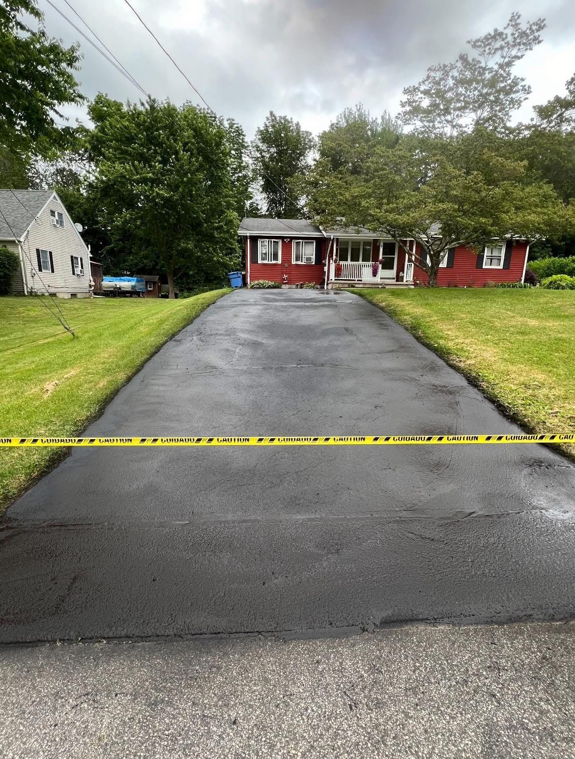 A residential property with a red house and a freshly paved black driveway blocked by yellow caution tape.