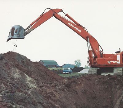 A large red excavator is digging in a pile of dirt