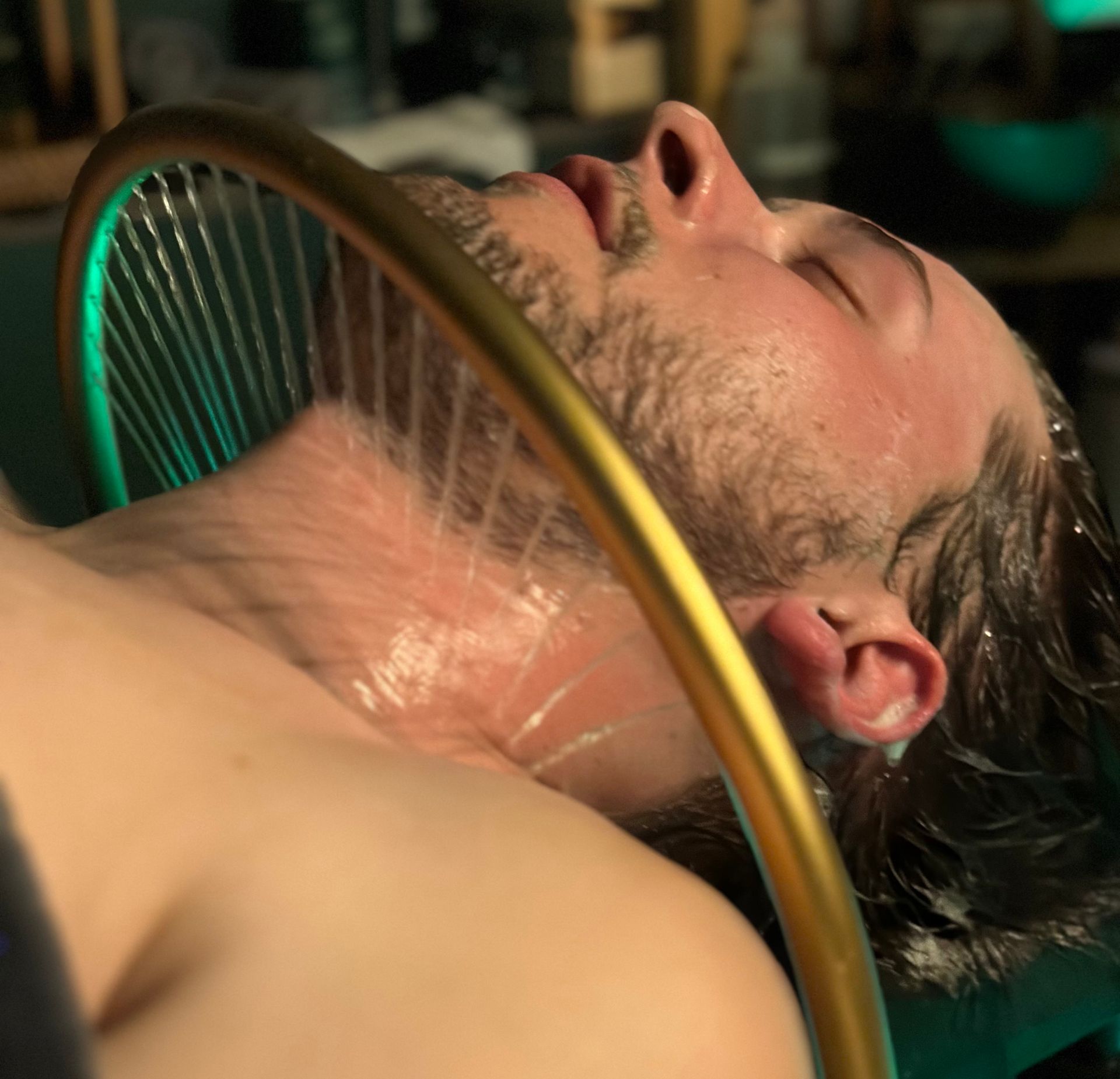 Man with eyes closed, wet from above; gold ring with wires around his neck.