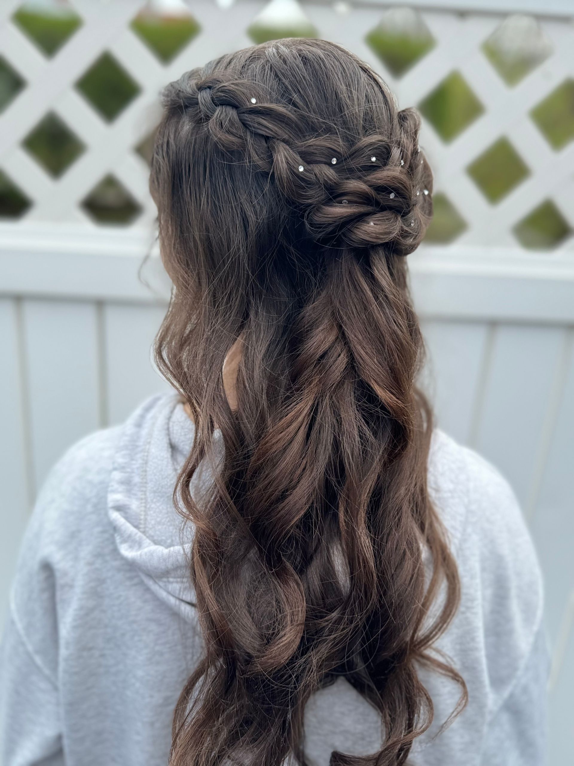 Woman with long, wavy brown hair styled in a half-up braid with small hair gems.