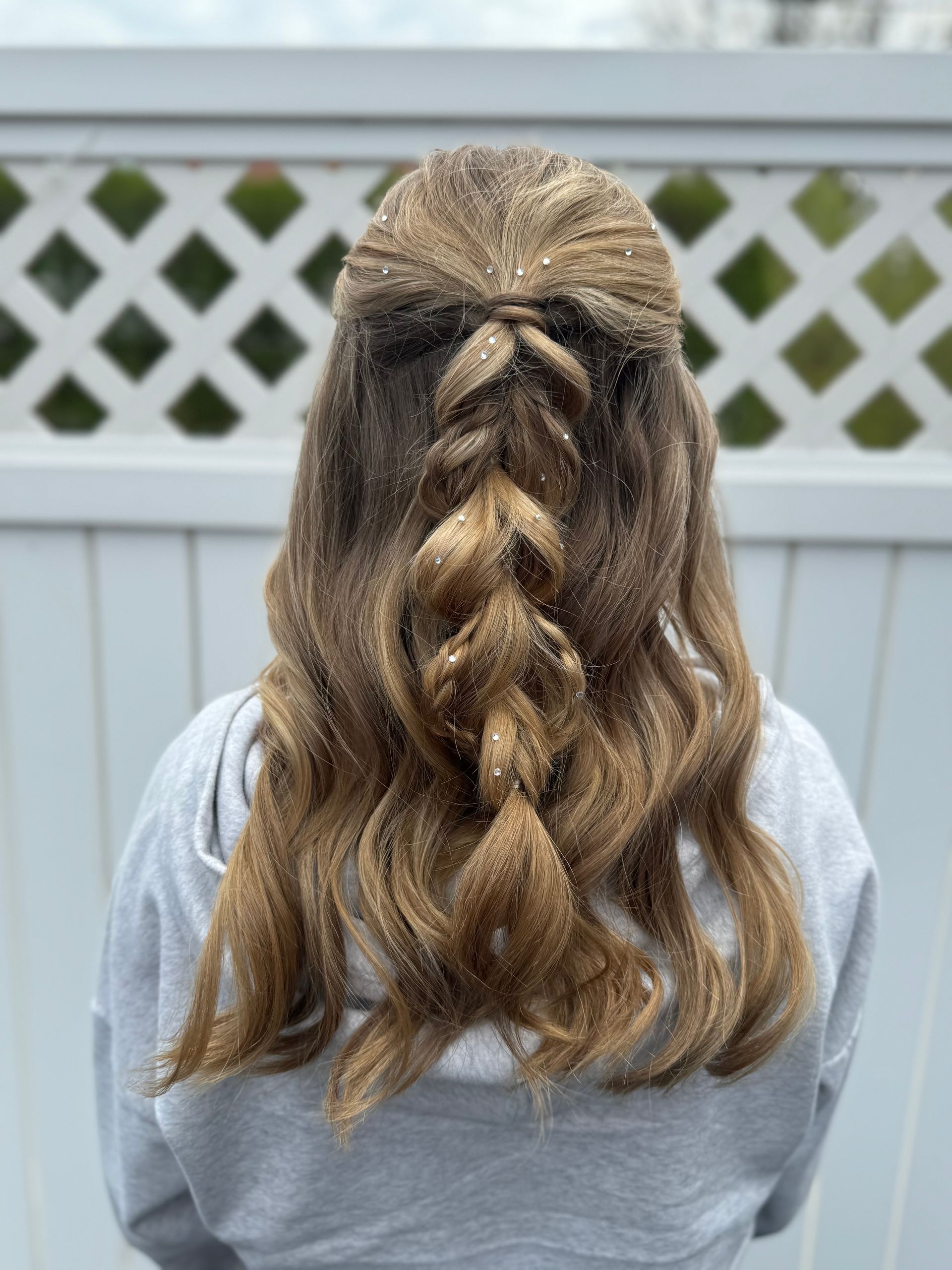 Woman with light brown, wavy hair styled with a half-up braid.