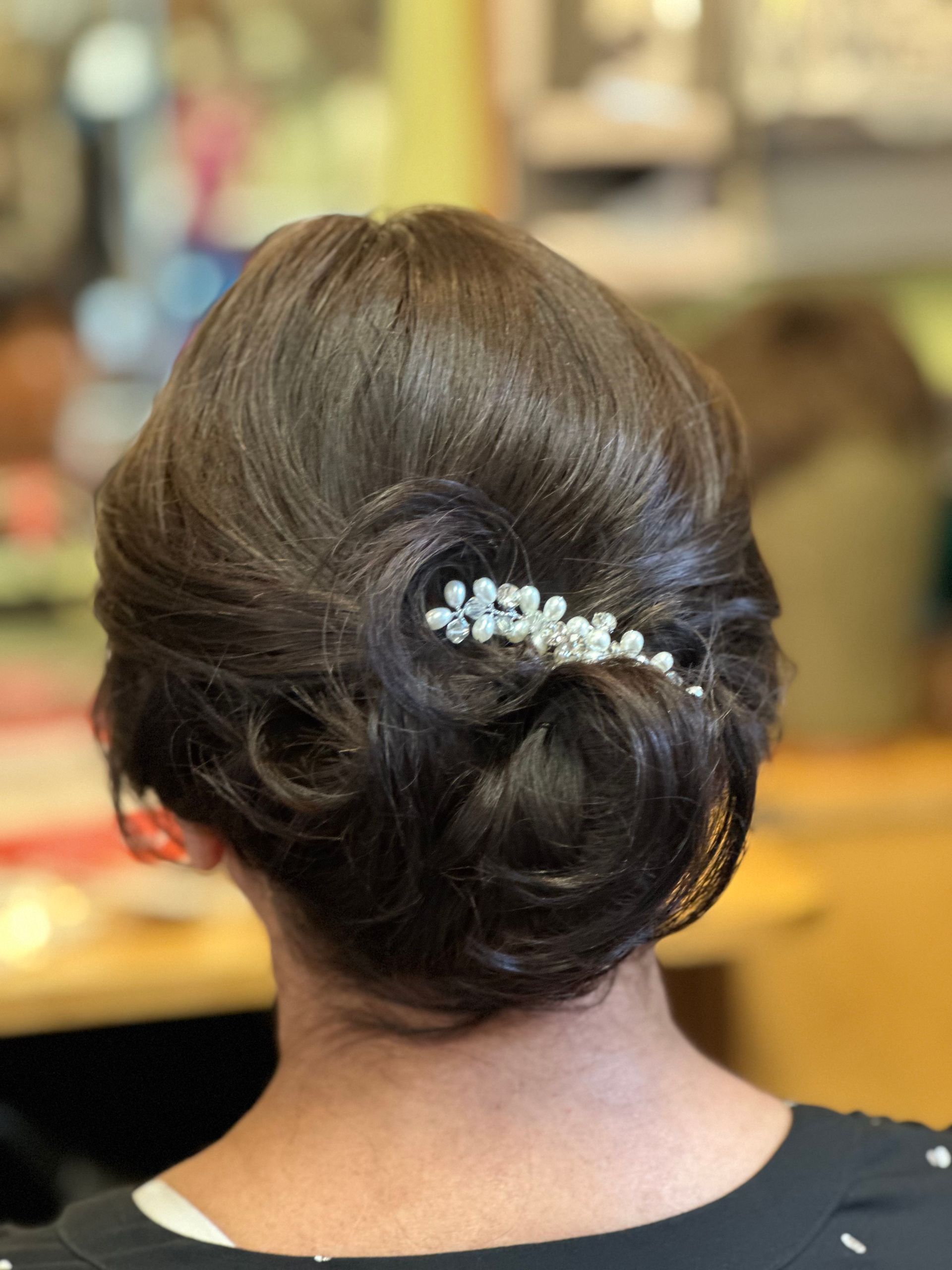 Woman with dark brown hair styled in an updo, adorned with a pearl hair clip.