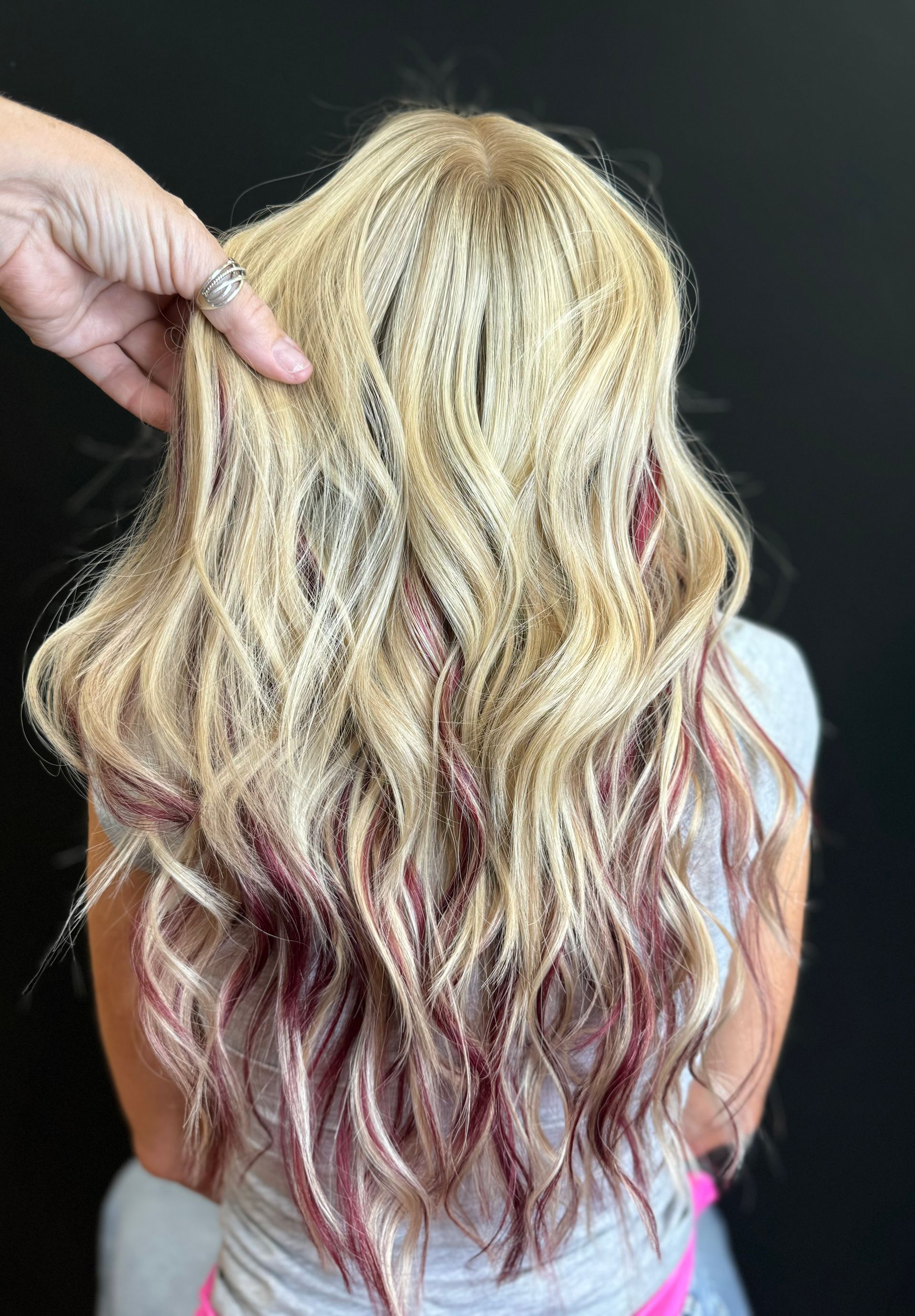 Blonde wavy hair with dark red highlights; hand touching hair, black background.