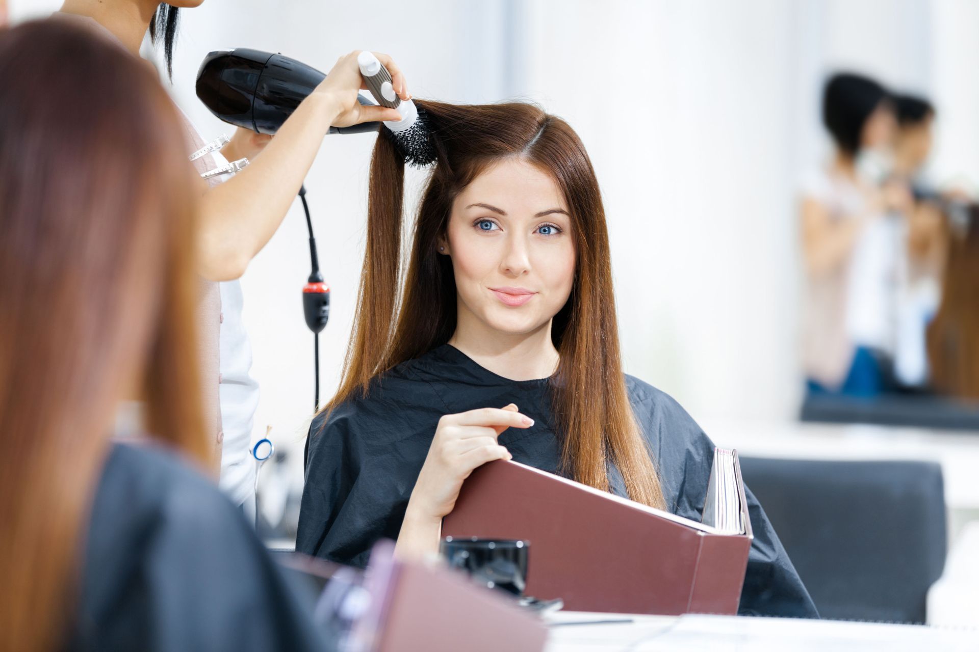 Woman getting a haircut at a salon, holding a magazine while stylist curls her hair