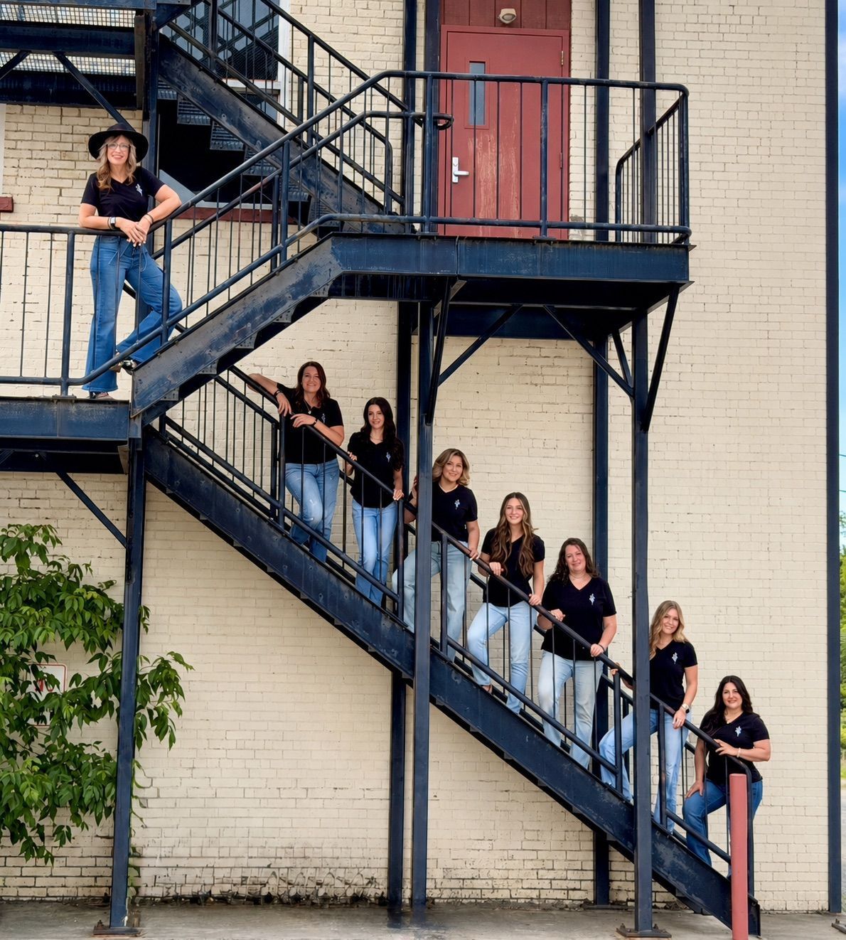 Group of people posing on an outdoor metal staircase beside a brick building.