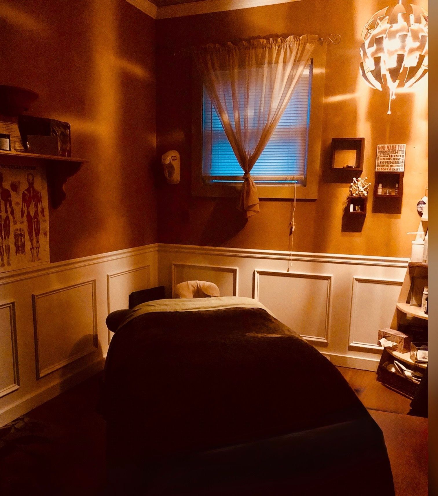 Cozy massage room with warm lighting, a table, window with curtains, and wall decor