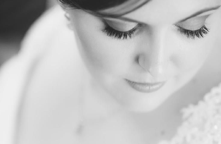 Close-up black-and-white portrait of a woman looking down with eyes closed, wearing a delicate dress.
