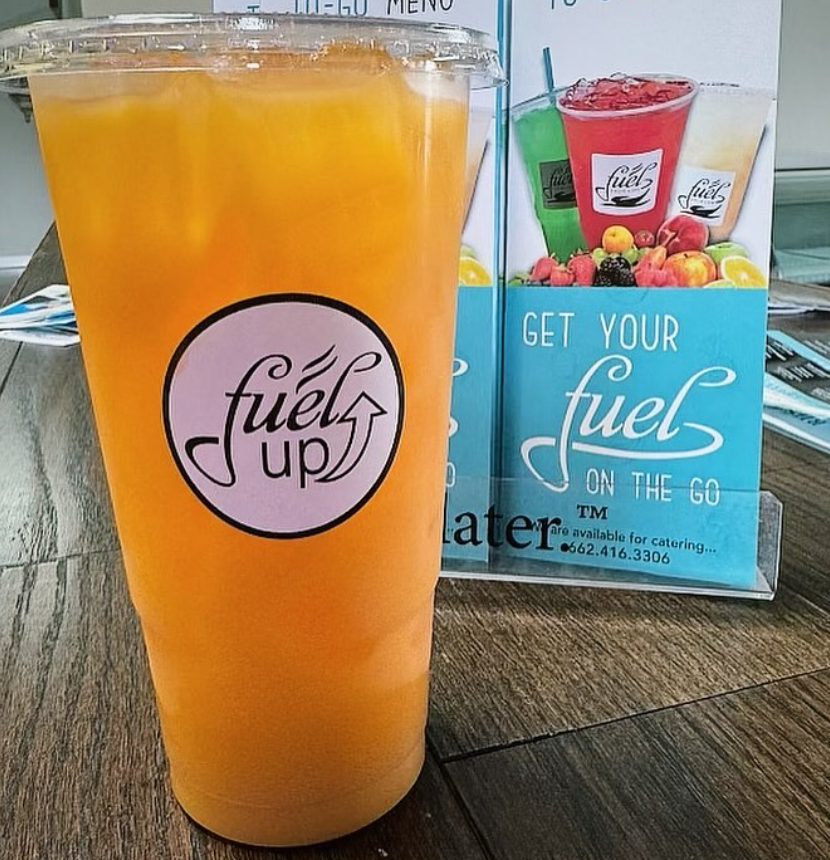 A cup of orange juice next to a sign that says get your fuel on the go