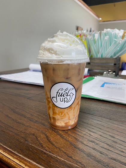 A cup of coffee with whipped cream on top is sitting on a wooden table.