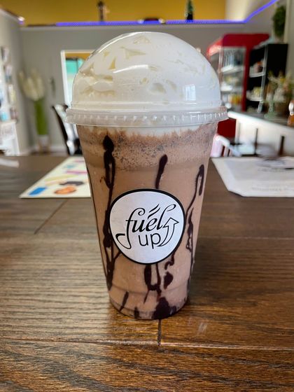 A cup of chocolate milkshake with whipped cream on top is on a wooden table.