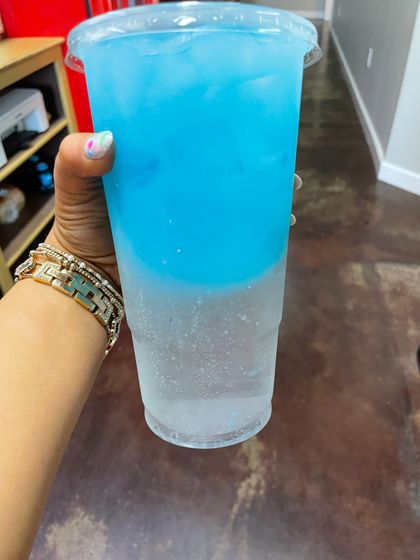 A person is holding a cup of blue liquid in their hand.