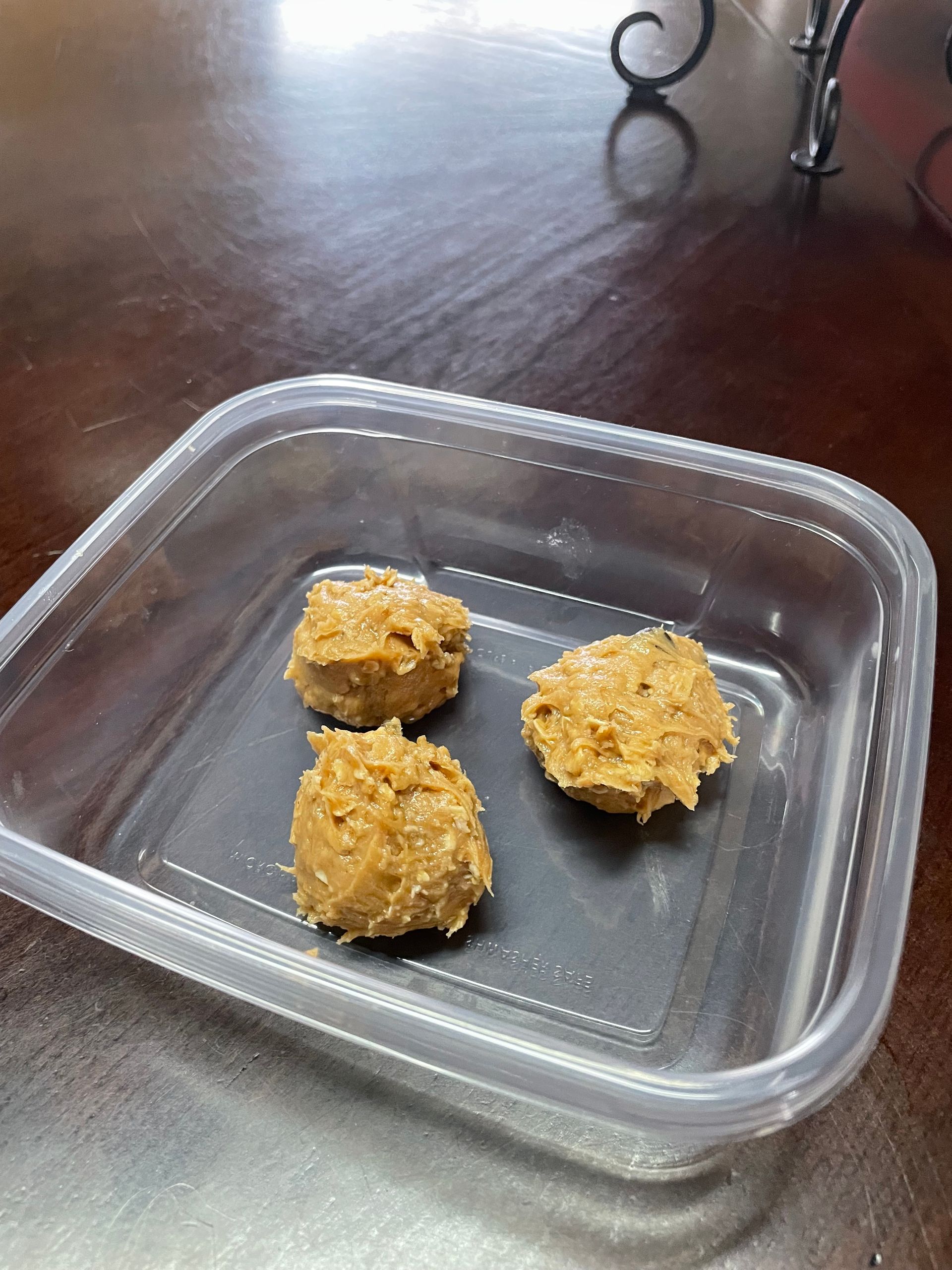 Three cookies are in a plastic container on a wooden table.