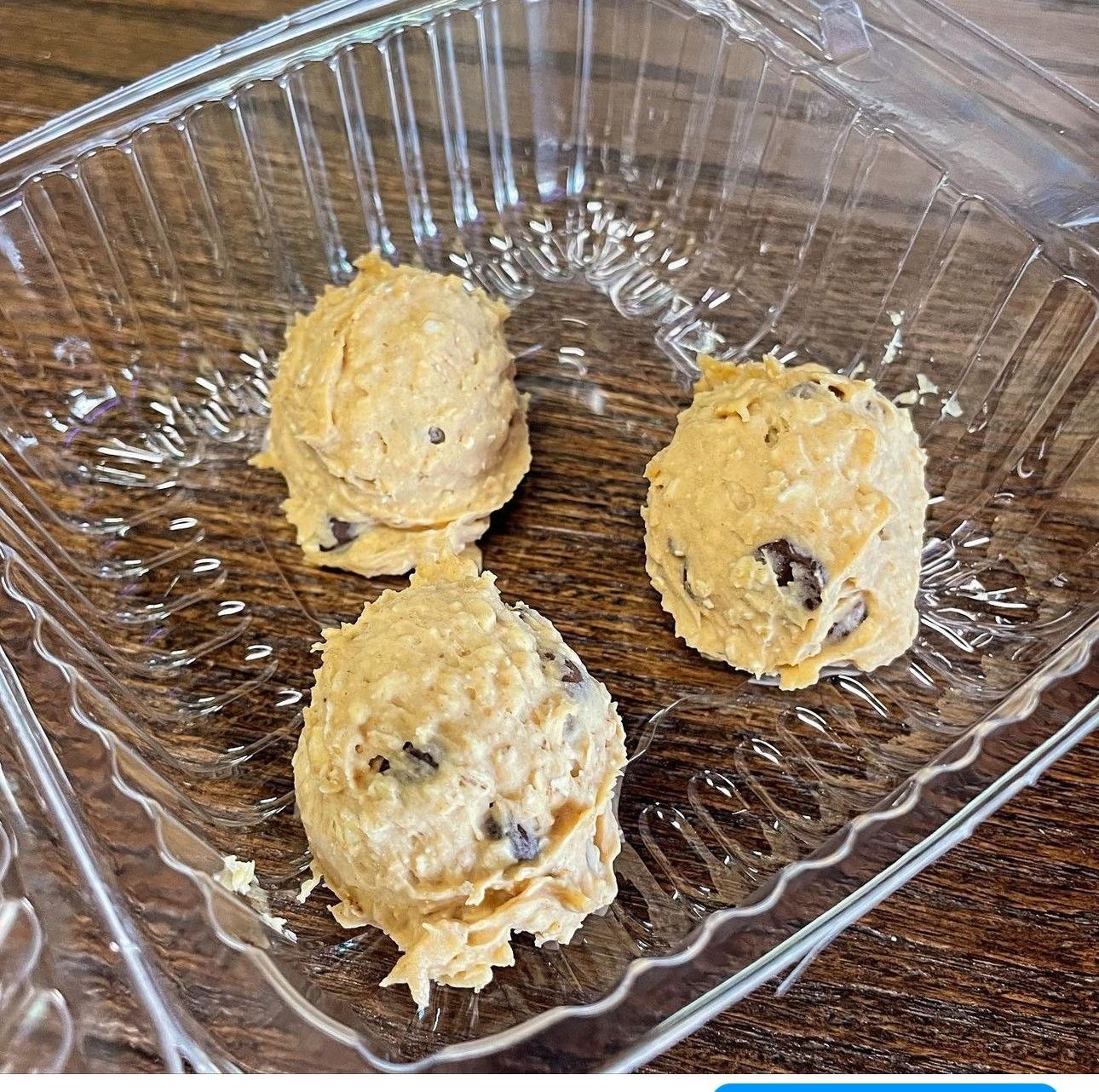 Three cookie dough balls in a plastic container on a wooden table.