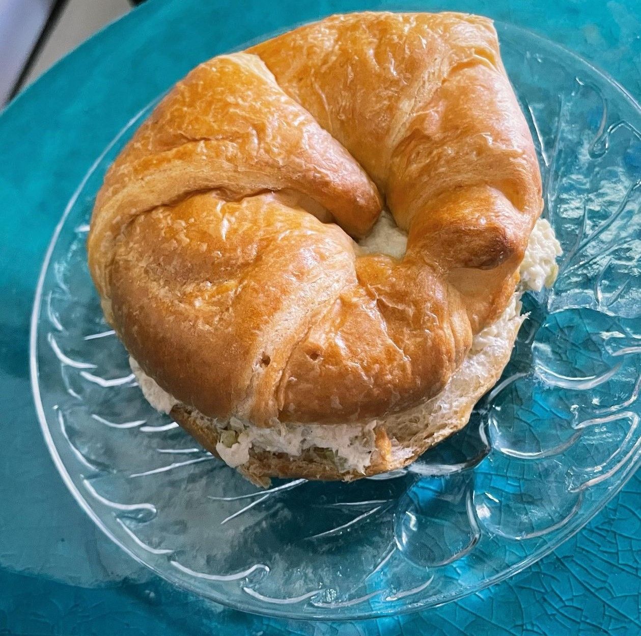 A croissant sandwich on a glass plate on a table