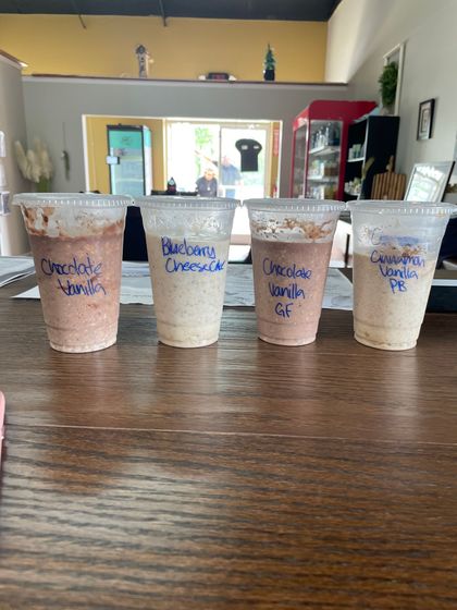 Four cups of different flavors of milkshakes are sitting on a wooden table.
