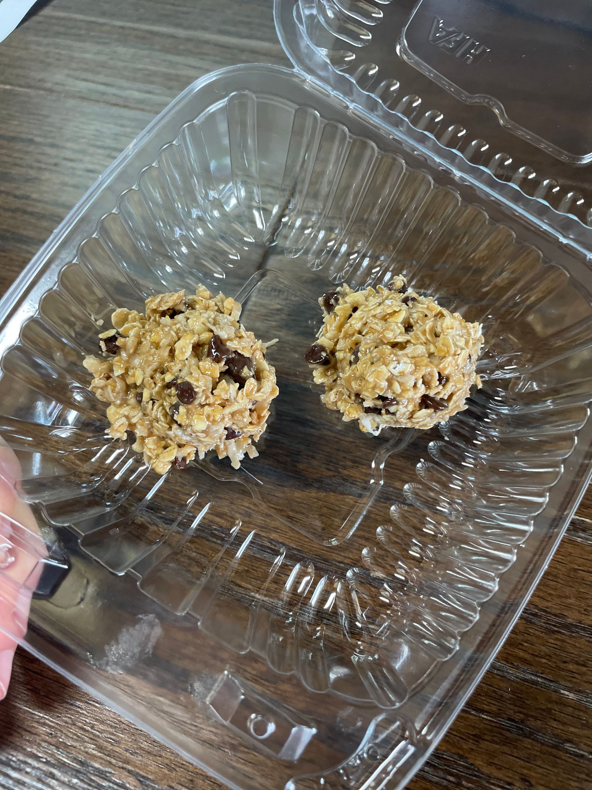 Two cookies in a plastic container on a wooden table.