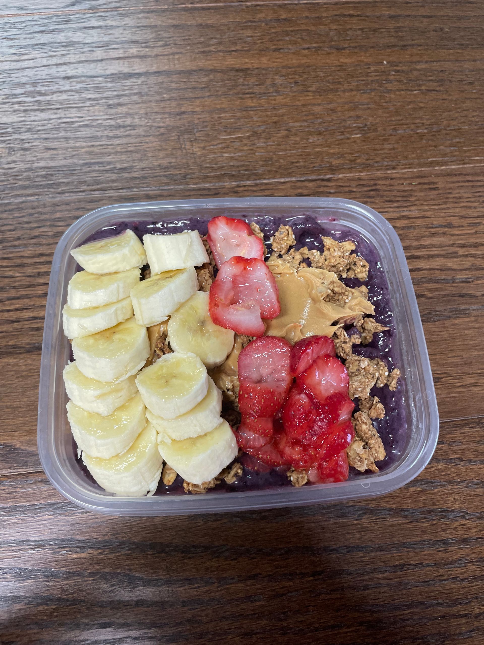 A plastic container filled with bananas , strawberries , peanut butter and granola.