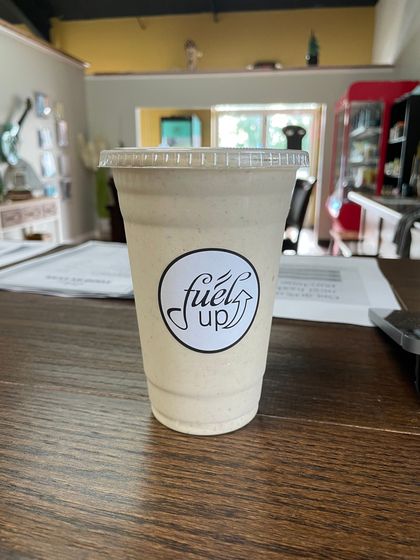 A cup of fuel up coffee is sitting on a wooden table.