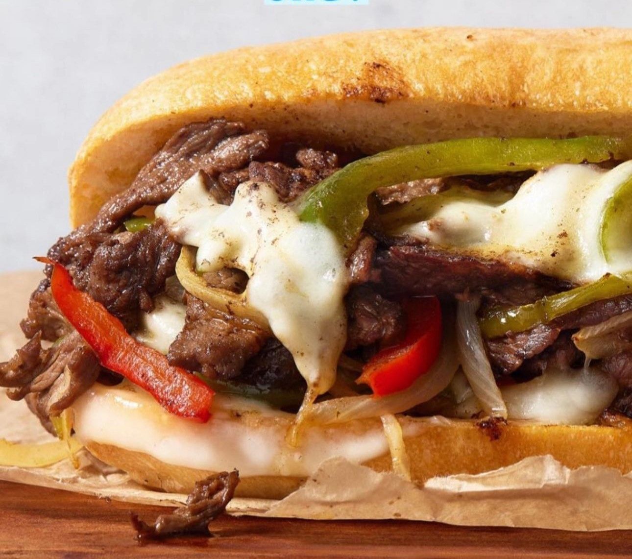 A close up of a steak sandwich with cheese and peppers on a cutting board.