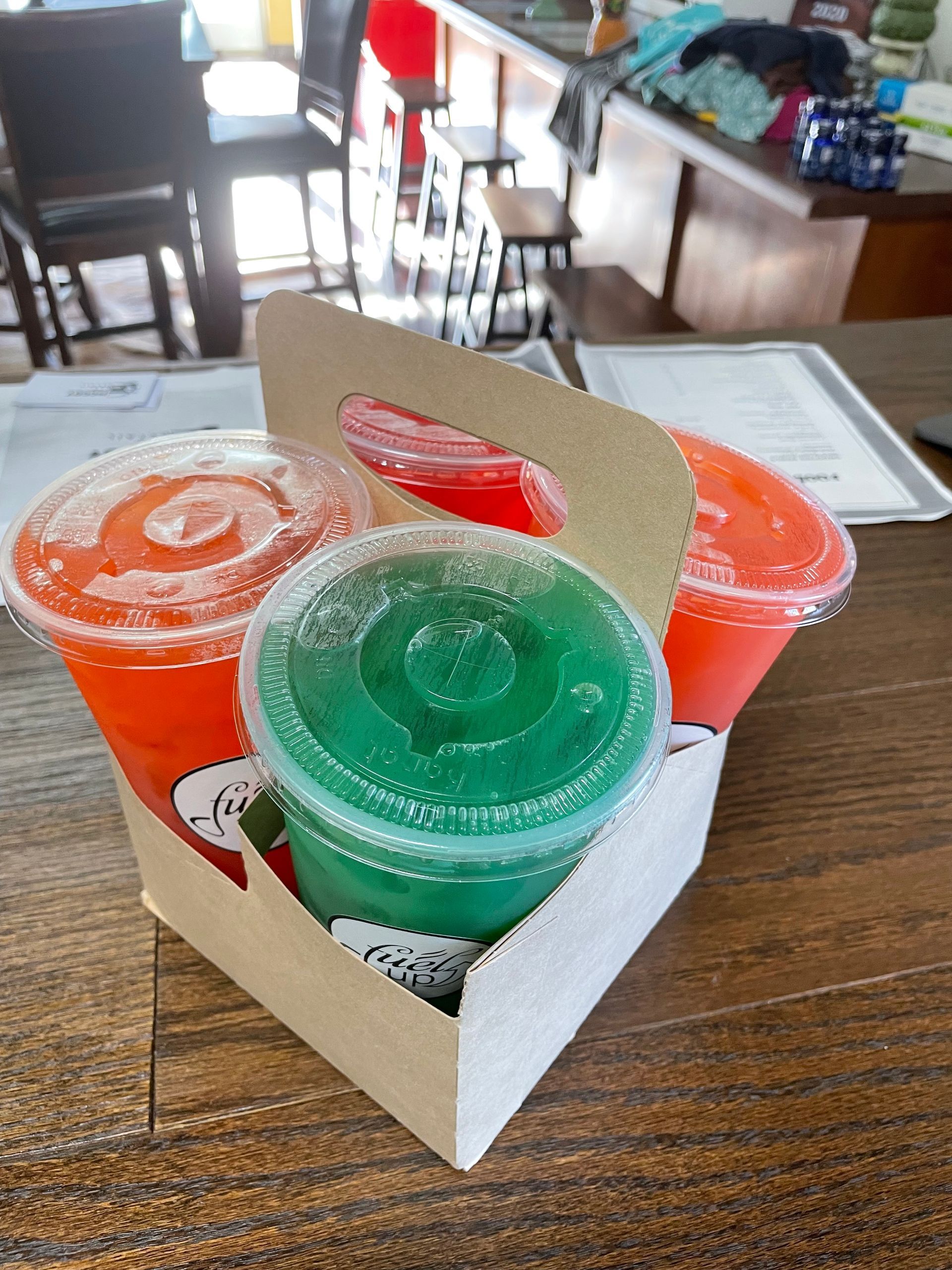 Three drinks are in a cardboard carrier on a wooden table.