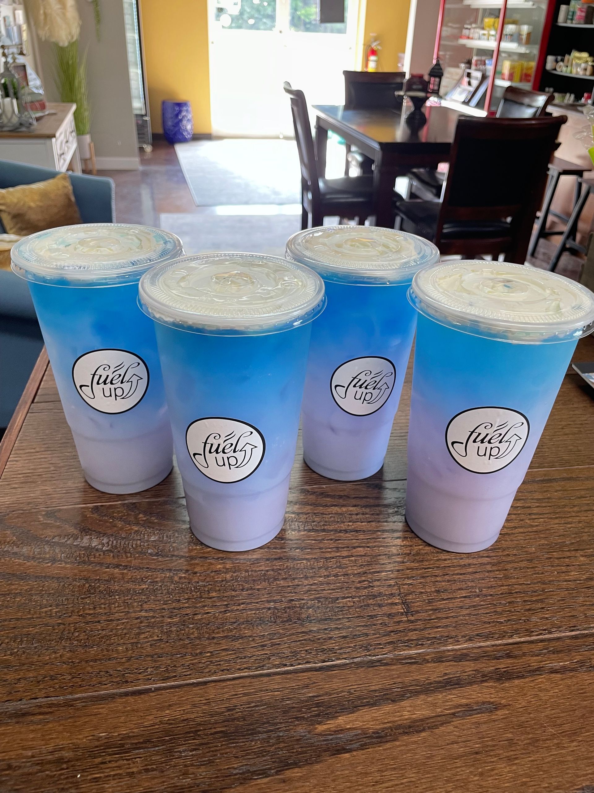 Four cups of blue and purple drinks are sitting on a wooden table.