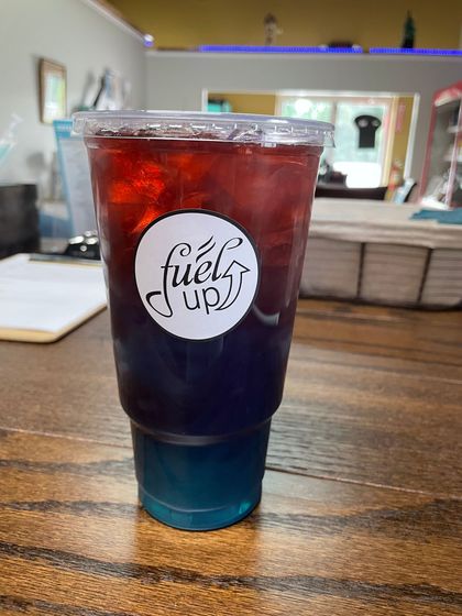 A cup of fuels up iced tea is sitting on a wooden table.