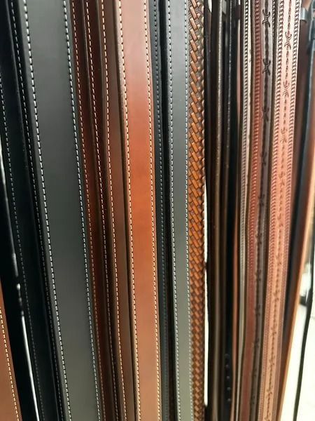 Close-up of vertically stacked leather belt or strap edges in black, brown, and tan.