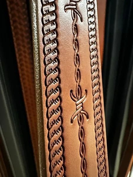 Close-up of a tan leather strap with decorative braided and stitched trim