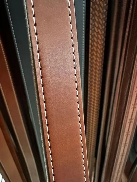 Close-up of brown leather straps with visible white stitching between darker leather panels
