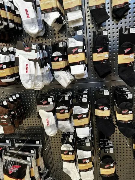 Socks displayed on a store pegboard, mostly white, black, and beige pairs in plastic packaging.
