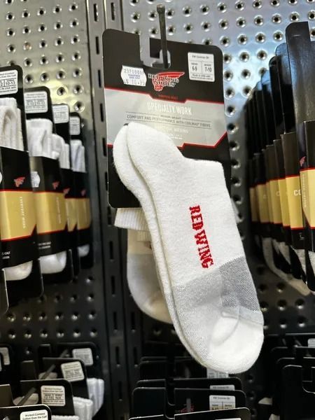 White Madden ankle sock displayed on a store pegboard rack, with red logo text and black-and-gold packaging nearby