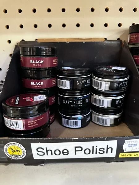 Shoe polish jars in black, navy, and brown on a shelf with a “Shoe Polish” label.