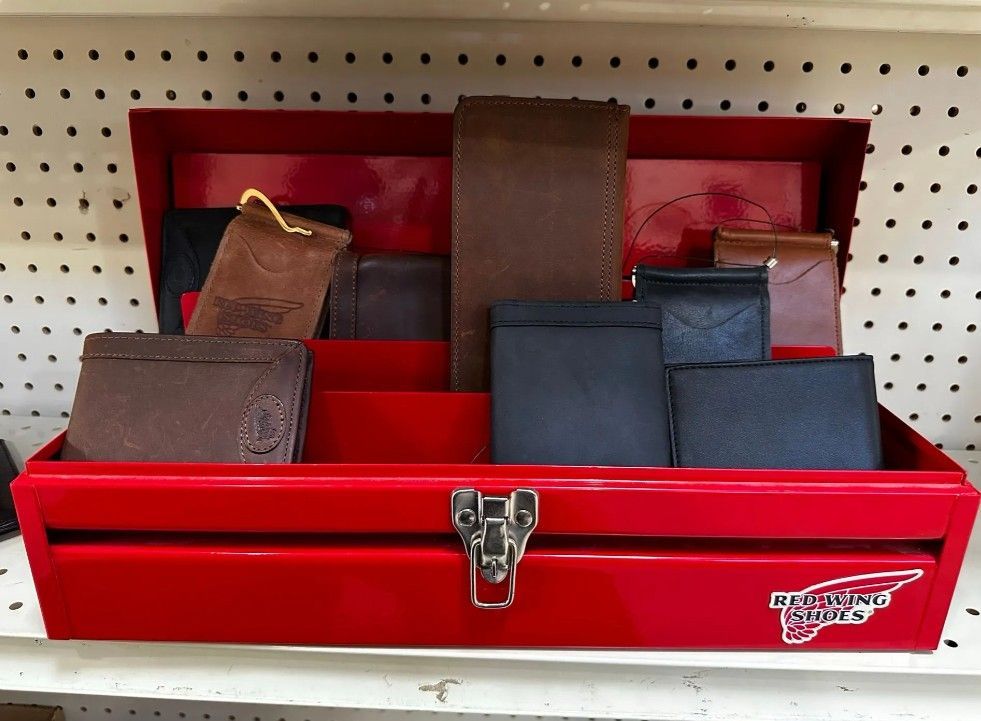 Red metal toolbox on a pegboard shelf holding several brown and black wallets or small cases