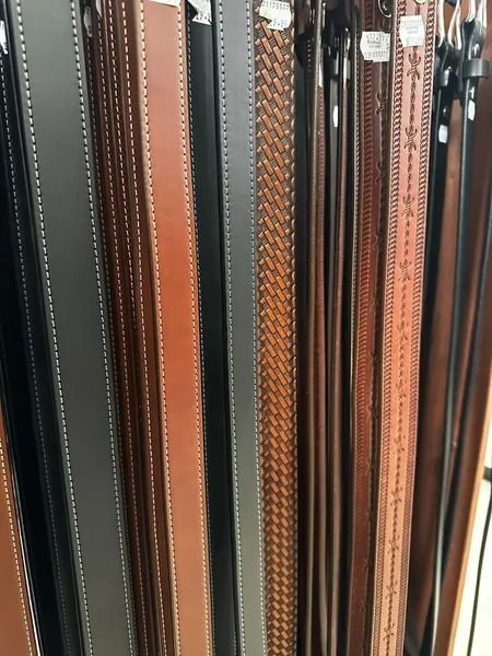 Assorted leather straps and belts hanging vertically in a shop display