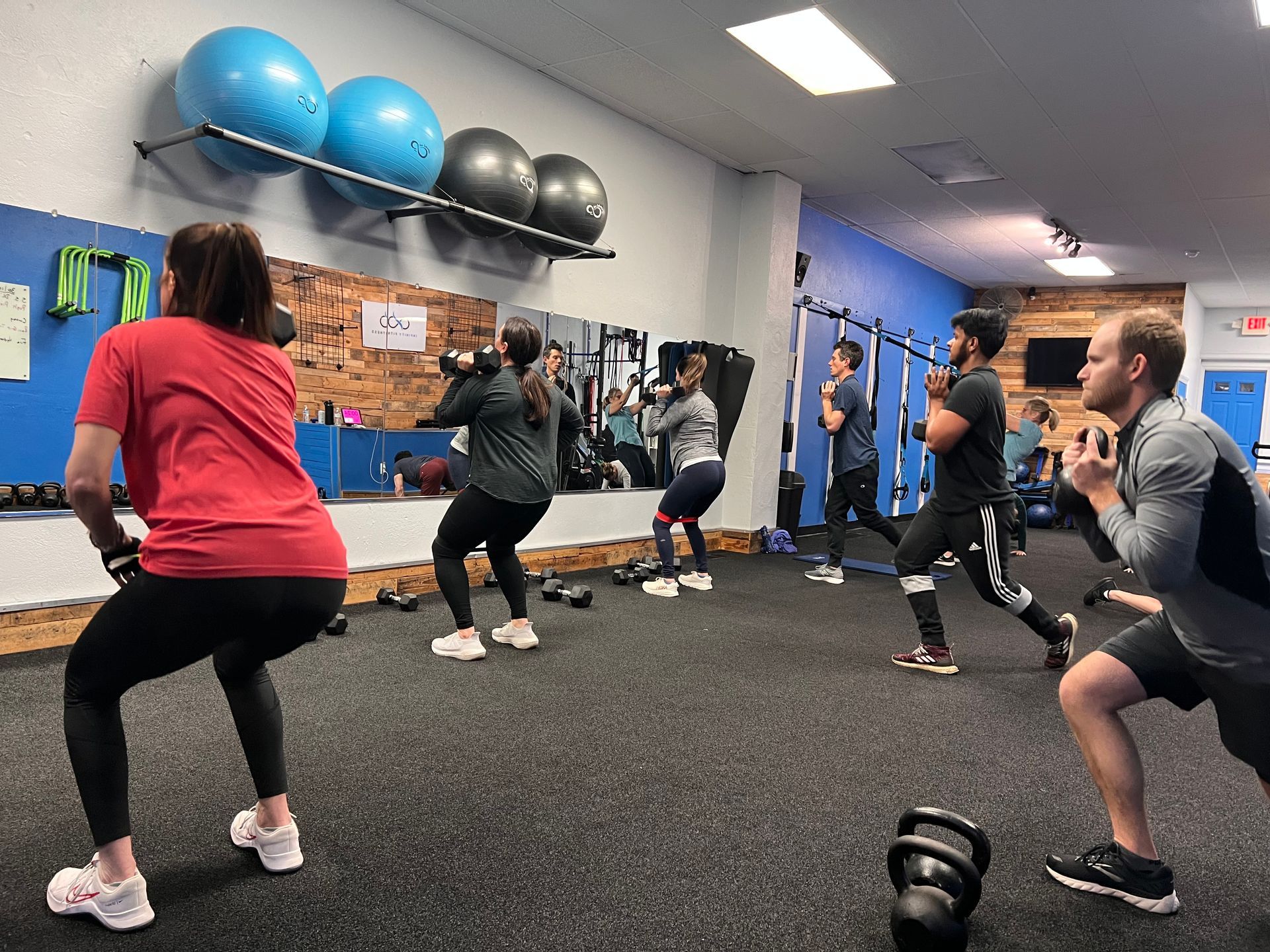 People in a gym, exercising with weights. Black flooring, blue and white walls.