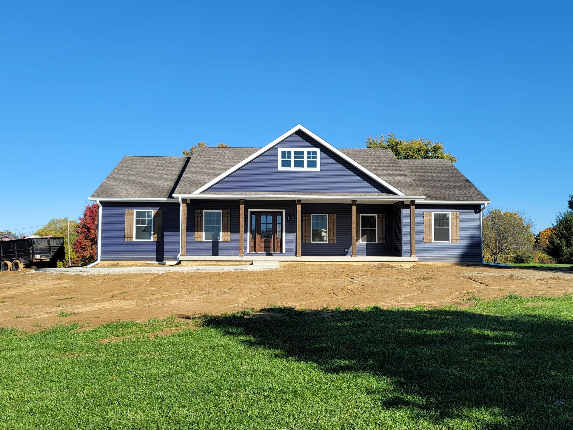 A blue house with a porch is sitting on top of a lush green field.
