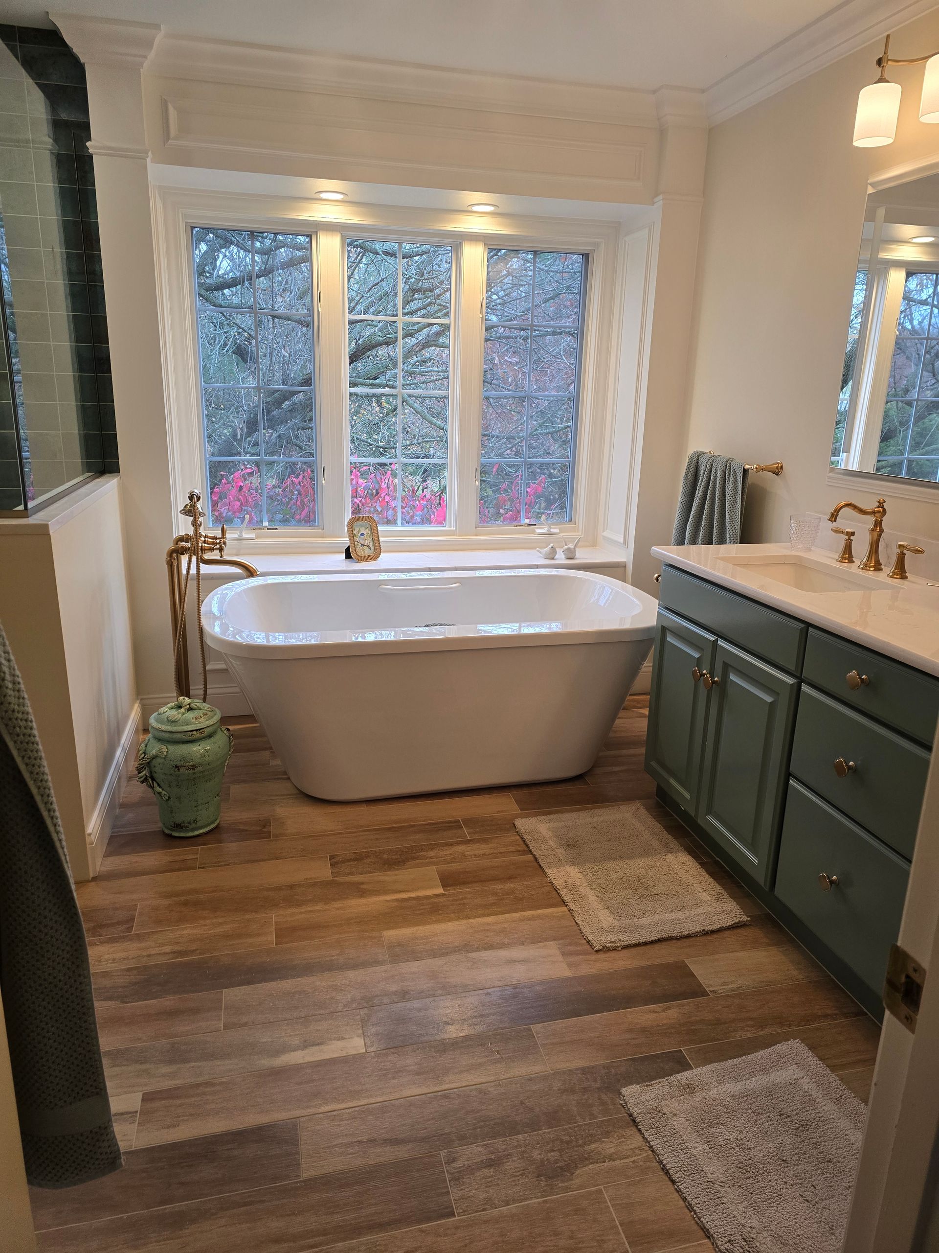 A bathroom with a tub , sink , mirror and window.