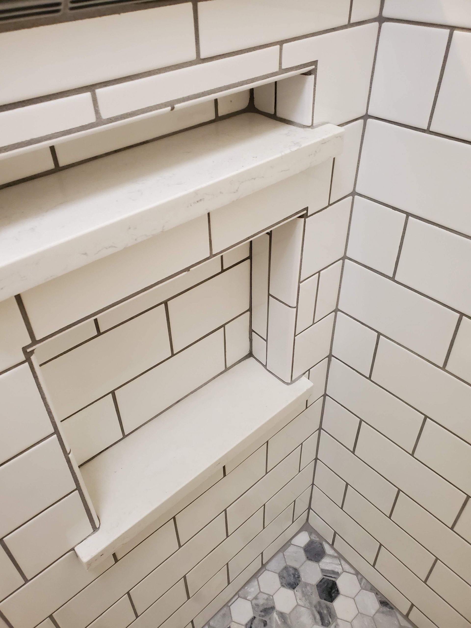 A shower with white tiles and a shelf in the corner
