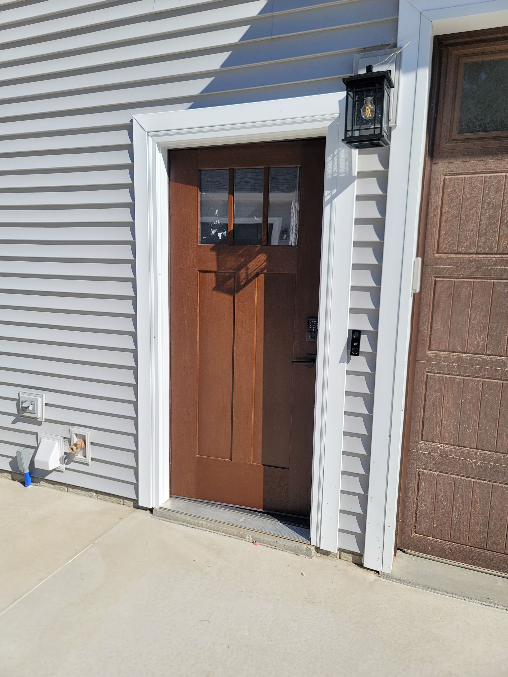A brown door is sitting on the side of a house next to a garage door.
