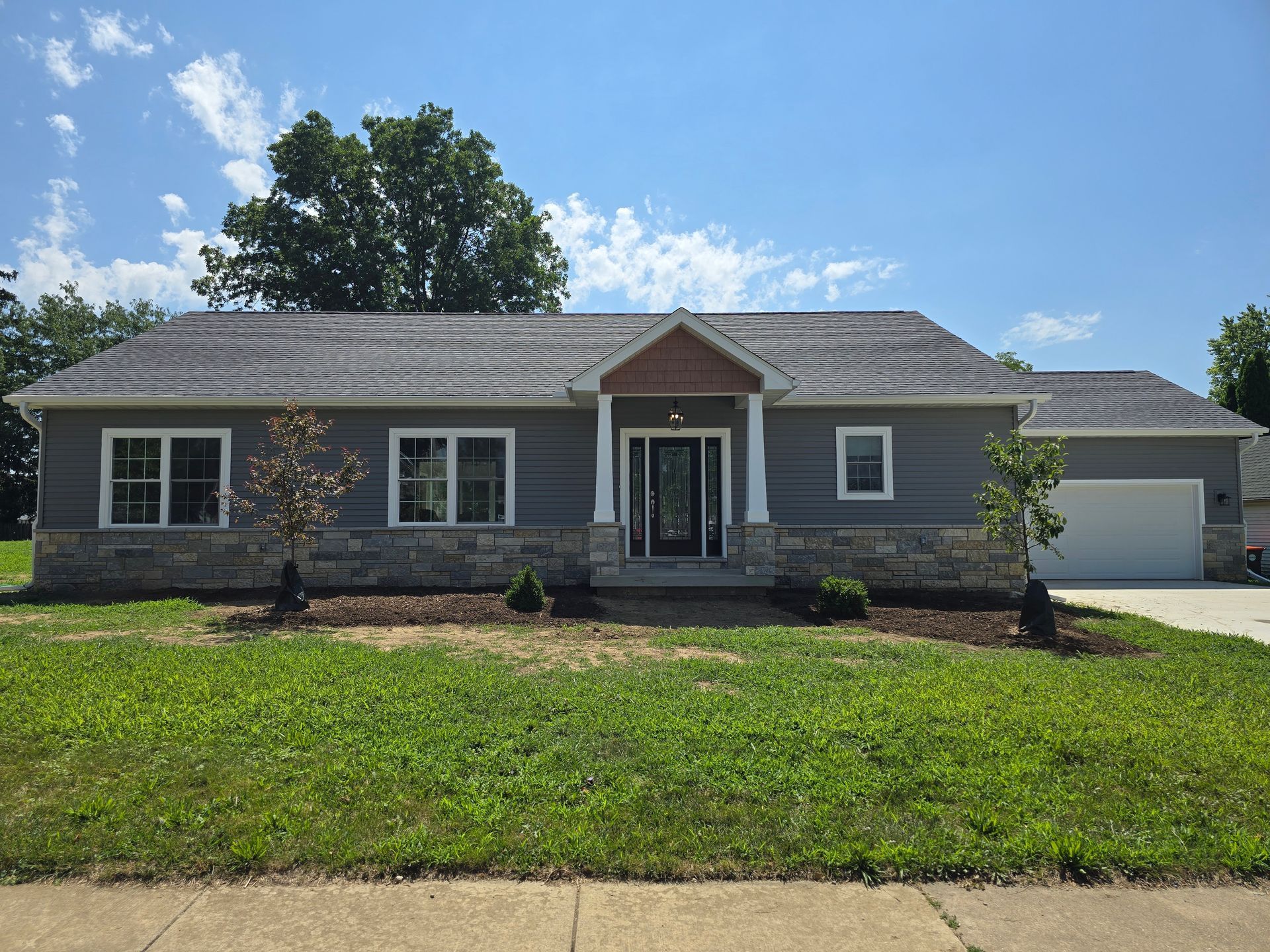 Gray house with stone accents, windows, and a front door under a small covered porch.