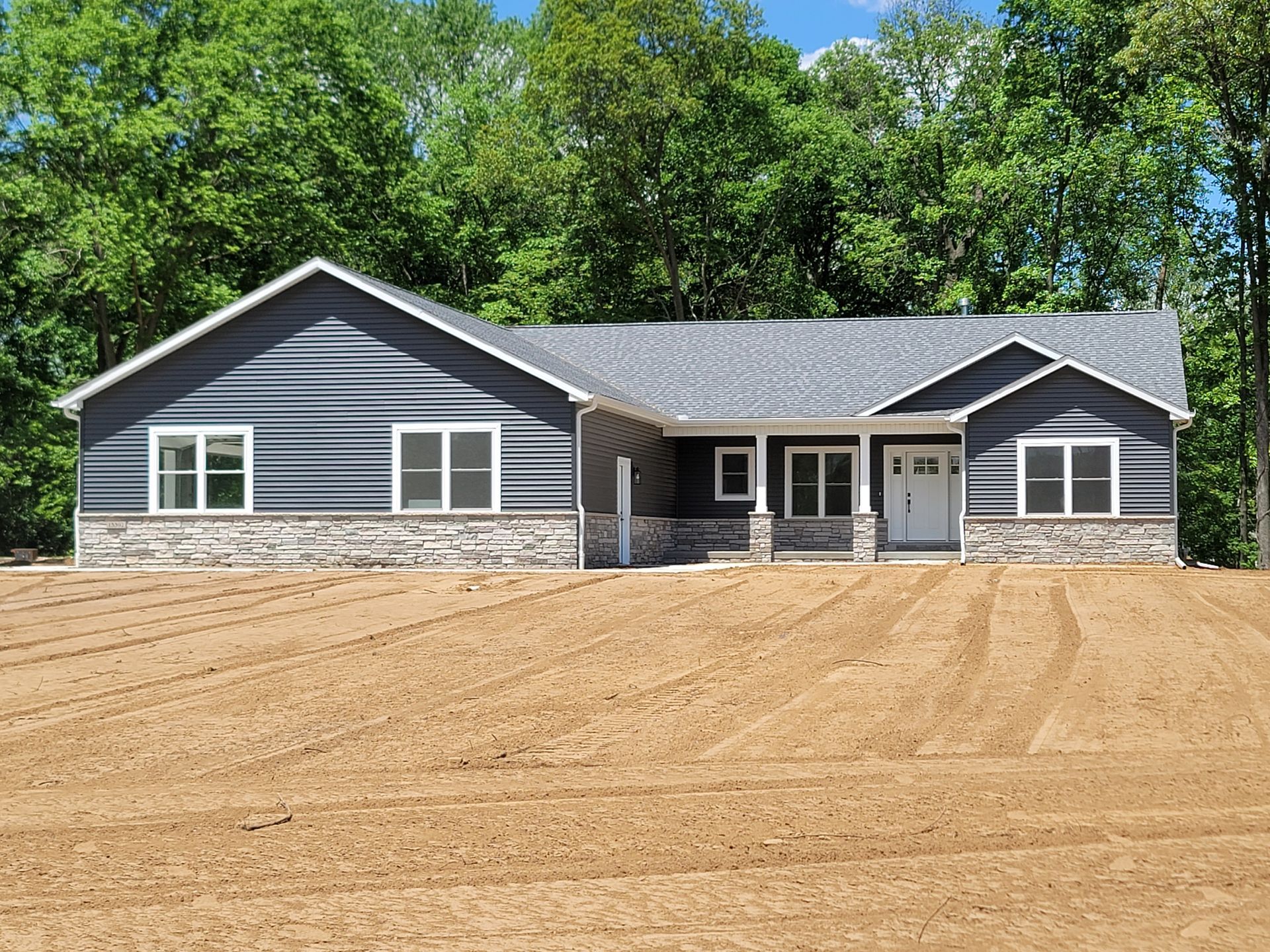 A large house is sitting on top of a dirt field surrounded by trees.